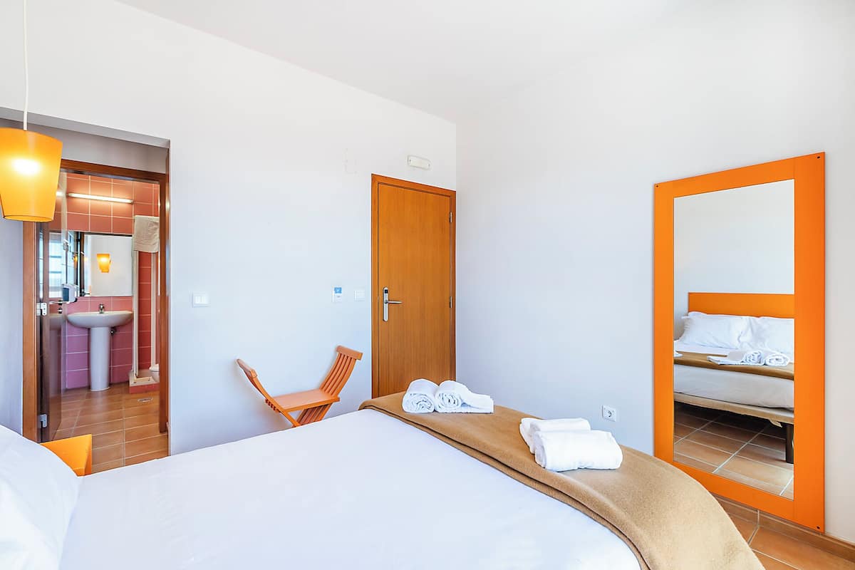 Una habitación de hotel con cama, una silla, baño con lavabo y espejo.