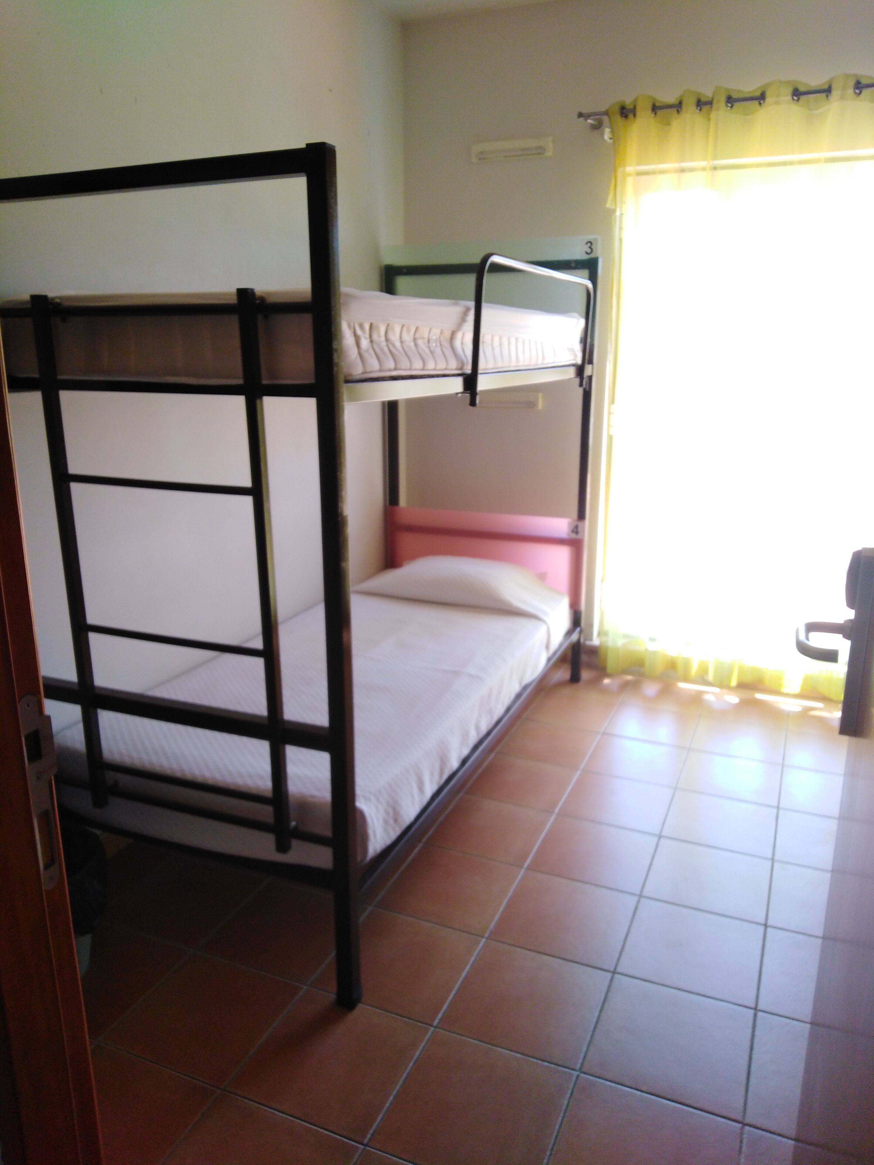 Habitación con literas, suelo de baldosas y una ventana con cortinas amarillas.