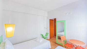 A hotel room with a bed, a small table, two chairs, a hanging light fixture, and a door leading to another room.