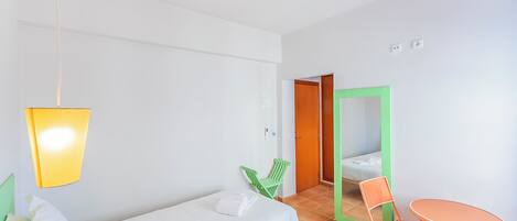 A hotel room with a bed, a small table, two chairs, a hanging light fixture, and a door leading to another room.