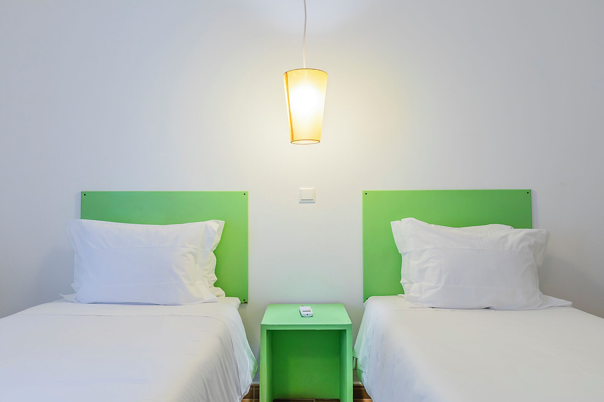 A room with two beds, each with a green headboard, a small green nightstand, and a wall-mounted light fixture.