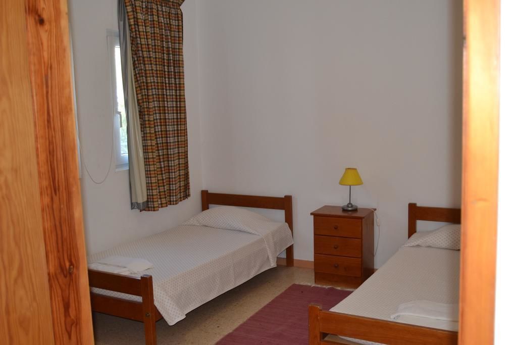 A small, simple room with two single beds, a wooden nightstand with a lamp, and a plaid curtain.