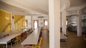 A long dining table with chairs, a kitchen area, and a decorative wall with a geometric pattern. - HI Alcoutim – Pousada de Juventude - Hostel (Alcoutim)