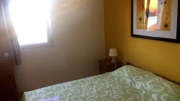 A room with a bed, a nightstand, a lamp, a window with curtains, and a framed picture on the wall.