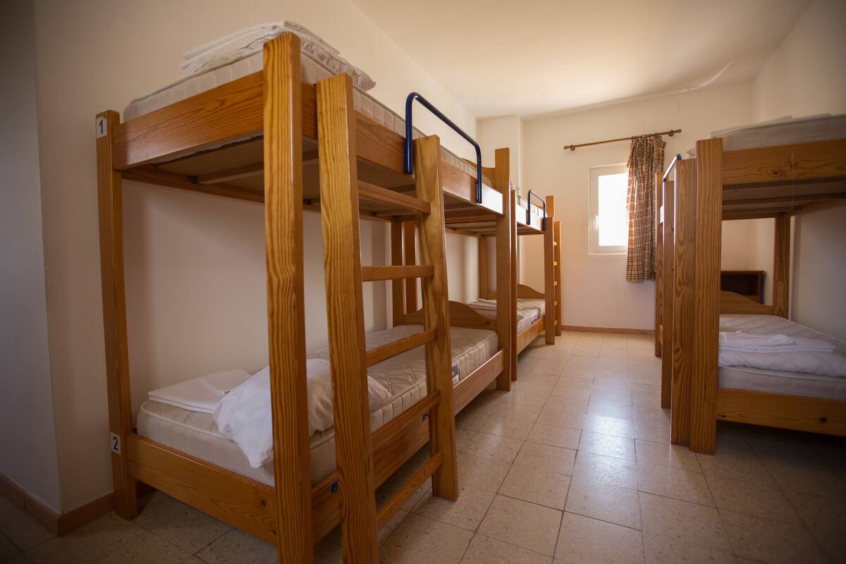 A dormitory room with bunk beds, a window with curtains, and a tiled floor.
