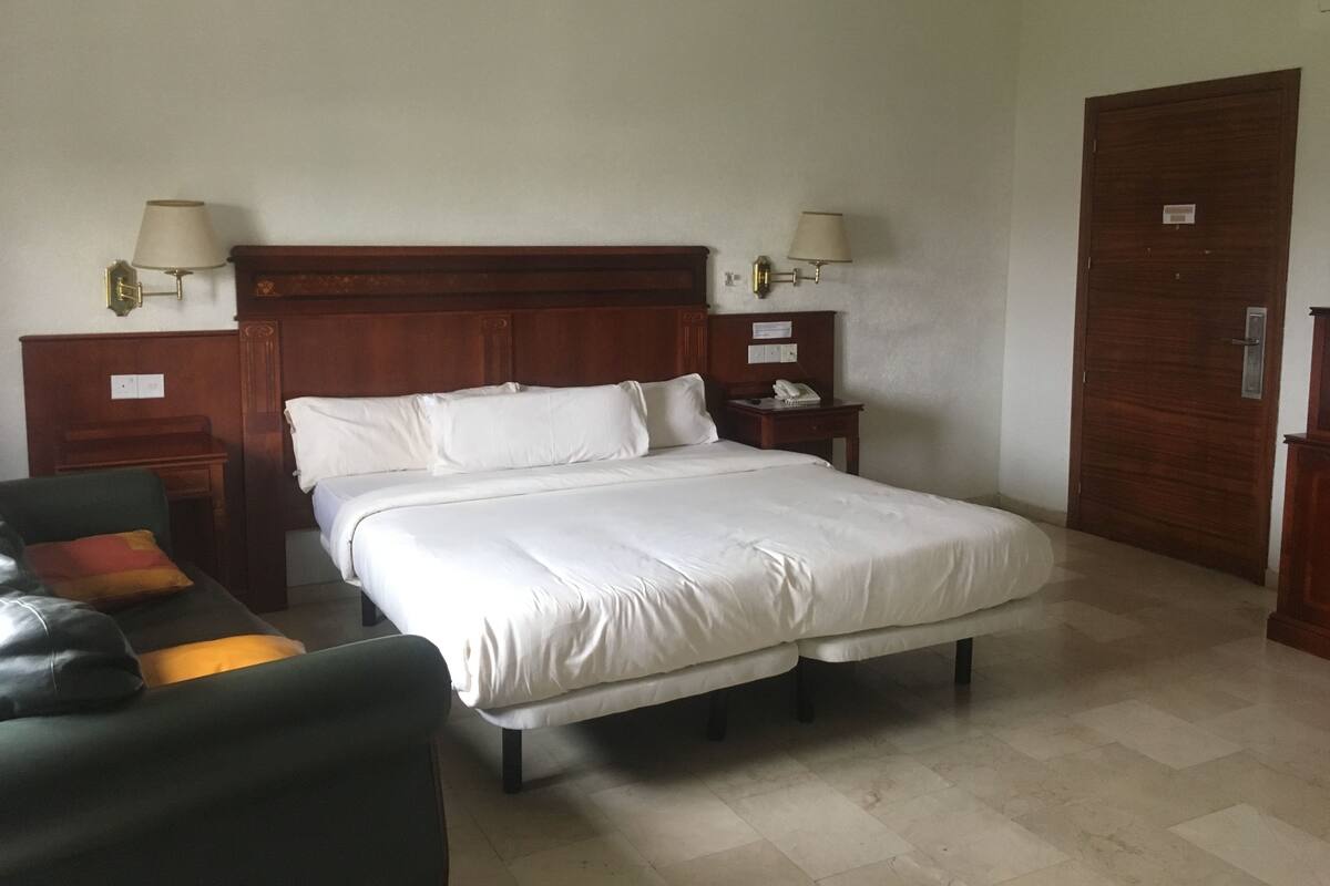 A hotel room with a double bed, two bedside tables, a desk, a chair, and a door.