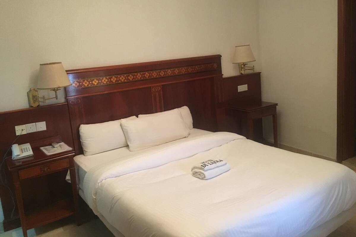 A hotel room with a wooden headboard, a bed with white linens, two bedside tables with lamps, and a telephone on the left table.