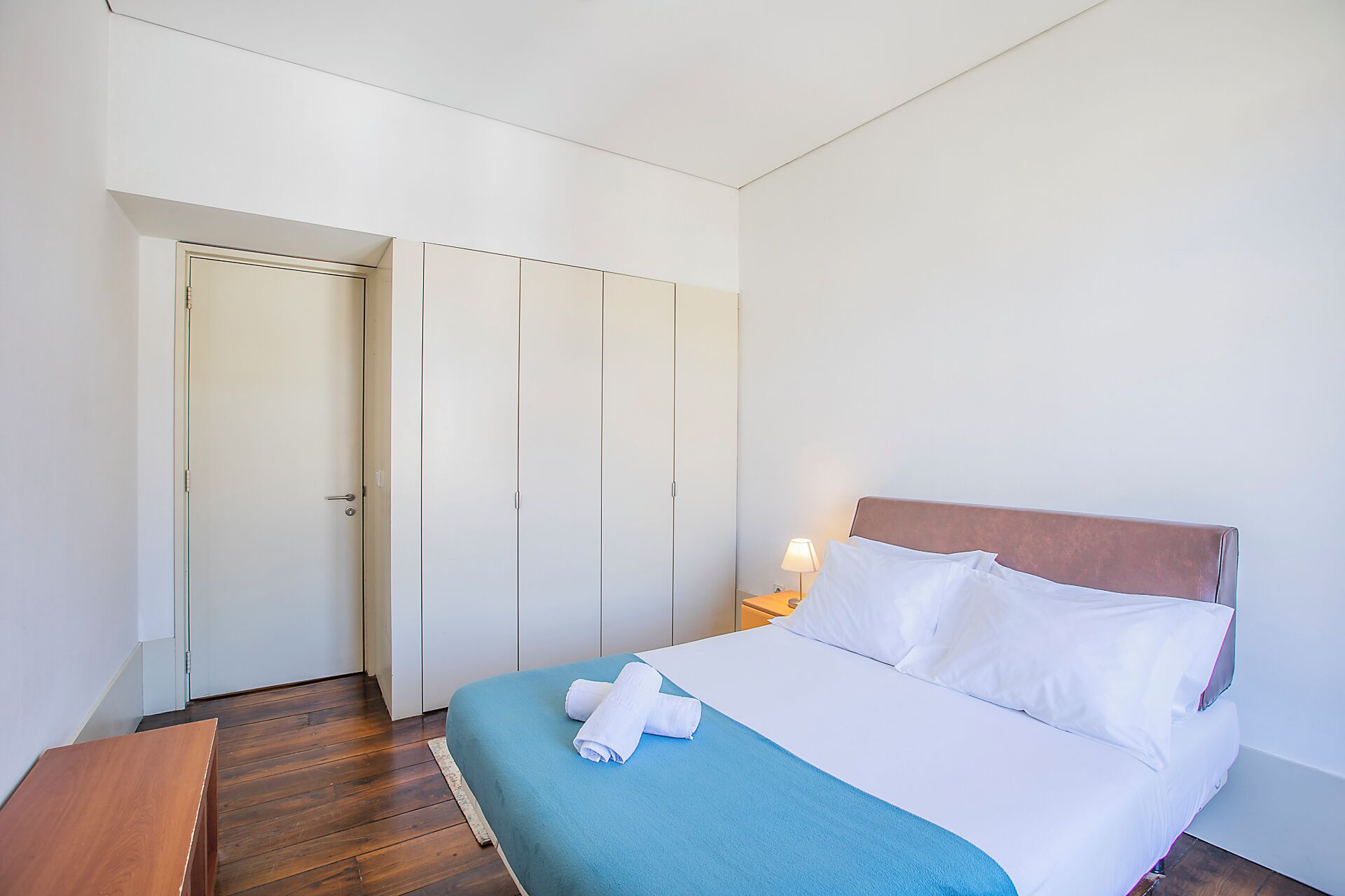 Una habitación de hotel con una cama, un banco de madera y un armario.