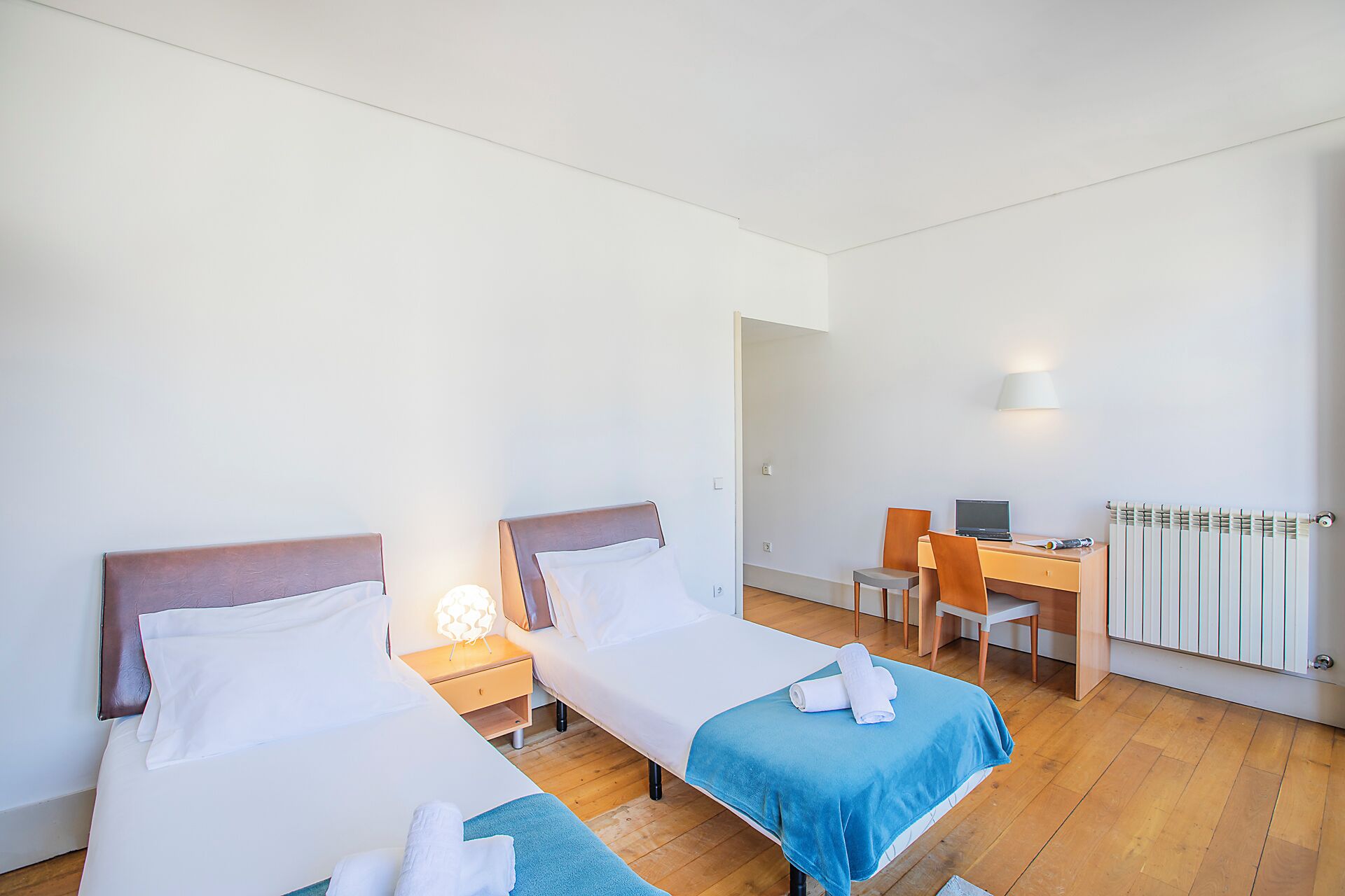 Een hotelkamer met twee bedden, een bureau, een stoel, een lamp en een radiator.