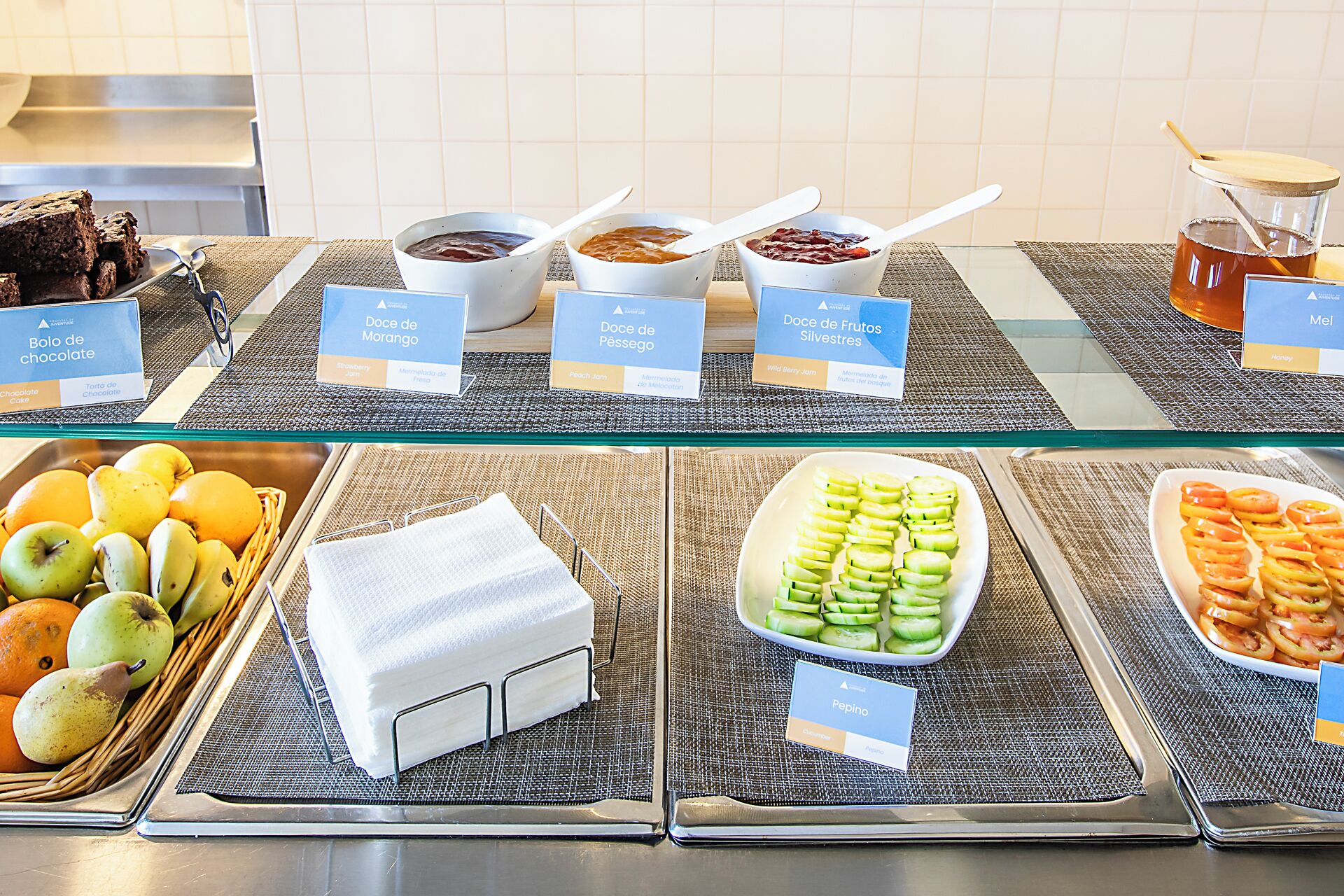 A buffet with labeled dishes including chocolate mousse, peach jelly, and sliced fruits.