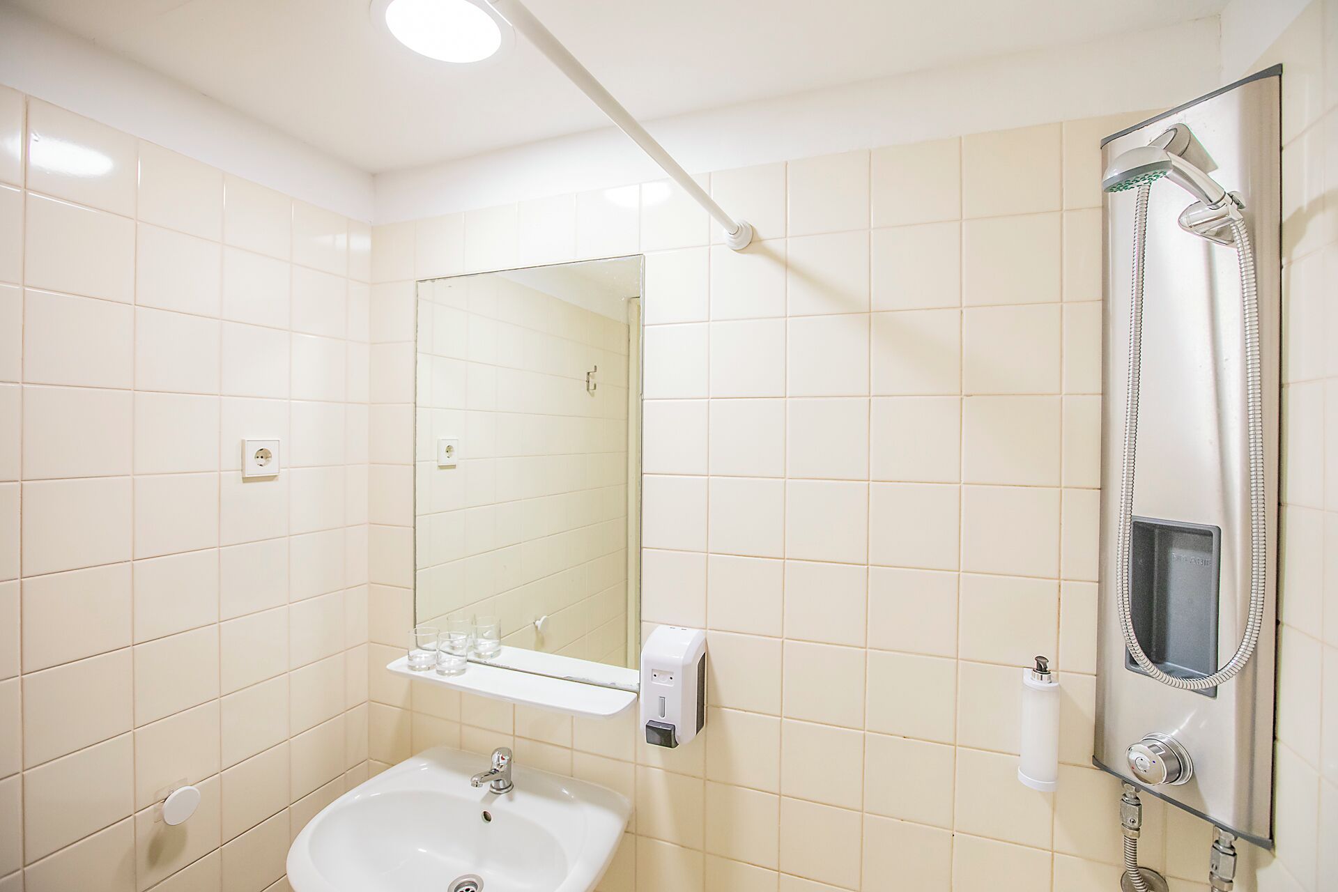 Baño con lavamanos, espejo y cabezal de ducha de mano.