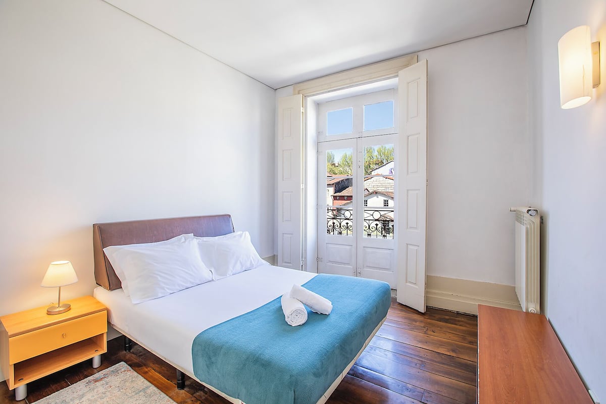 Un dormitorio con cama, mesita de noche, lámpara y vistas por una puerta.