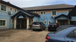 A building with a blue facade, multiple air conditioning units, and a parking area with several cars. - Marble Hill Hotel (Lagos)