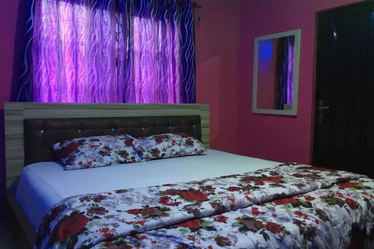 A bedroom with a bed, a headboard, a floral bedspread, a mirror, and curtains.