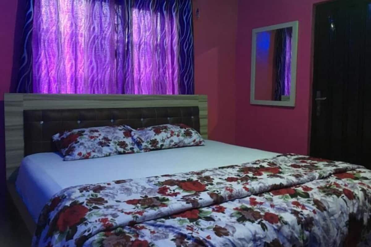 A bedroom with a bed, floral bedding, a headboard, a window with curtains, and a door.