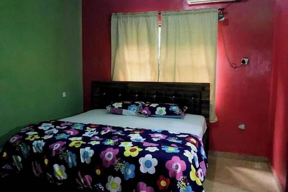 A bedroom with a bed, a window with curtains, and an air conditioning unit on the wall.