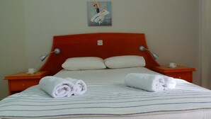 Una cama bien hecha con ropa de cama a rayas, dos almohadas y dos toallas enrolladas sobre una mesita de noche de madera.