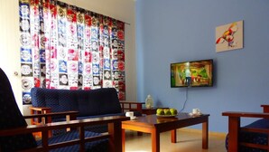 Una habitación con un sofá azul, una mesa de centro de madera y un televisor en la pared.