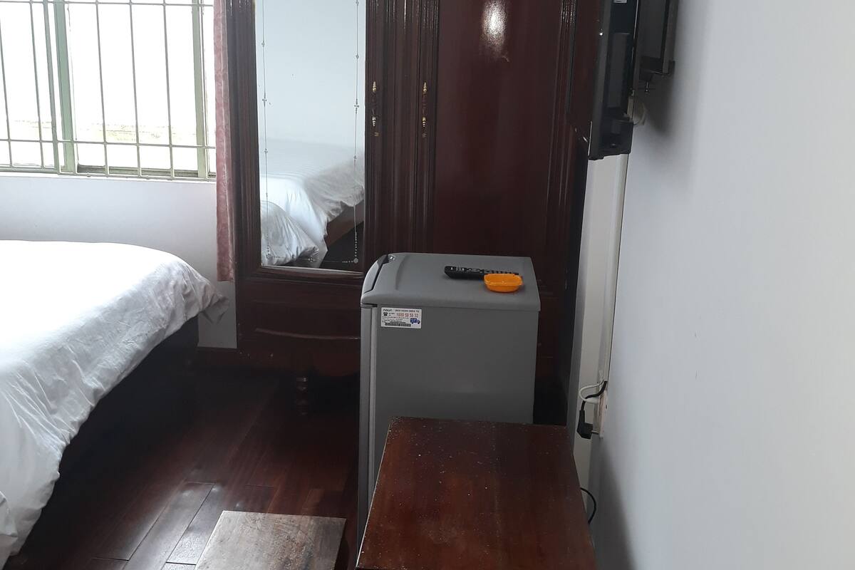 Una habitación con cama, armario, una mesita y un refrigerador.