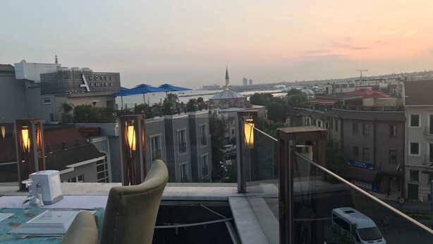 A rooftop terrace with a table set for dining, overlooking a cityscape with buildings and a river. - Fairytale Hotel (Istanbul)