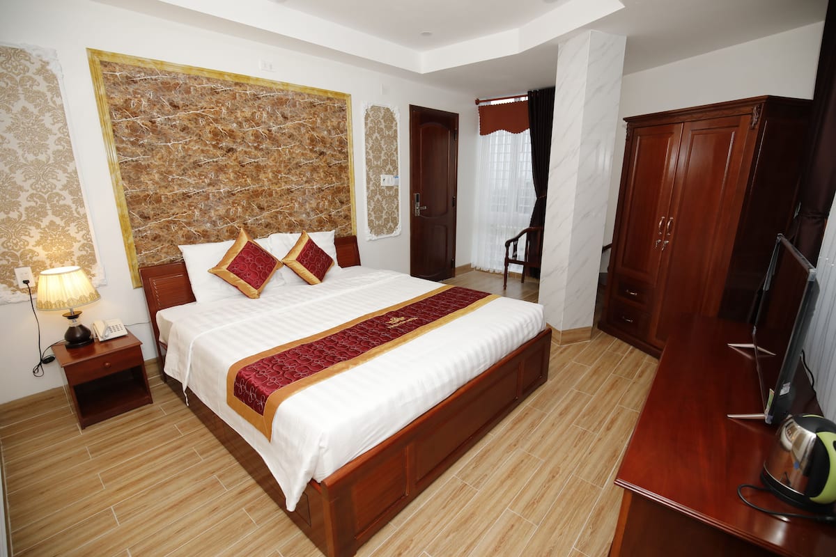 A hotel room with a large bed, wooden wardrobe, and a desk with a kettle.
