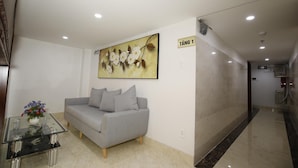 A modern lobby with a grey sofa, a glass coffee table with a vase of flowers, and a large floral painting on the wall. - Orange Quy Nhon (Quy Nhon Nam)