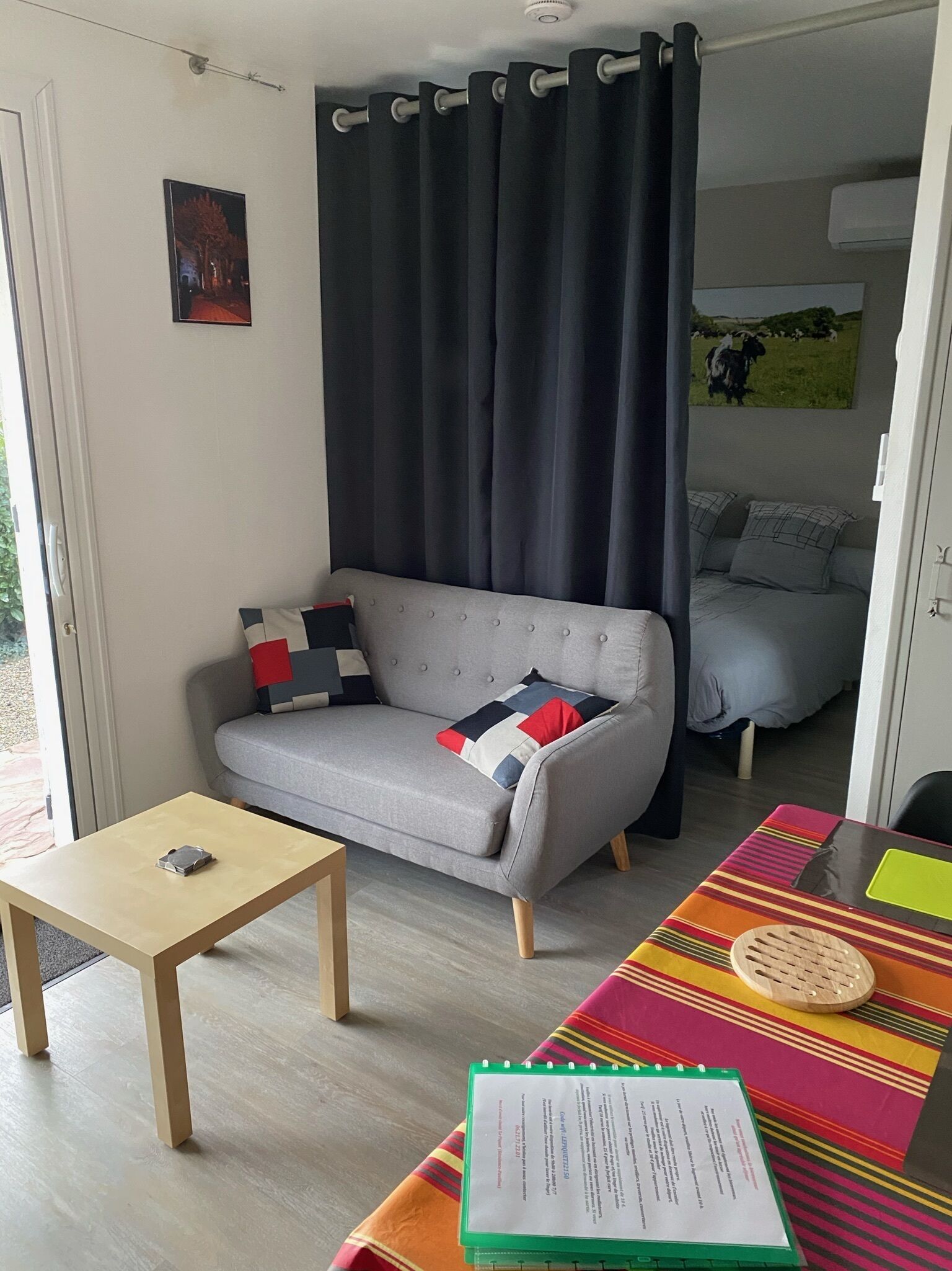 A cozy living room with a grey sofa, a small table, and a colorful striped tablecloth.