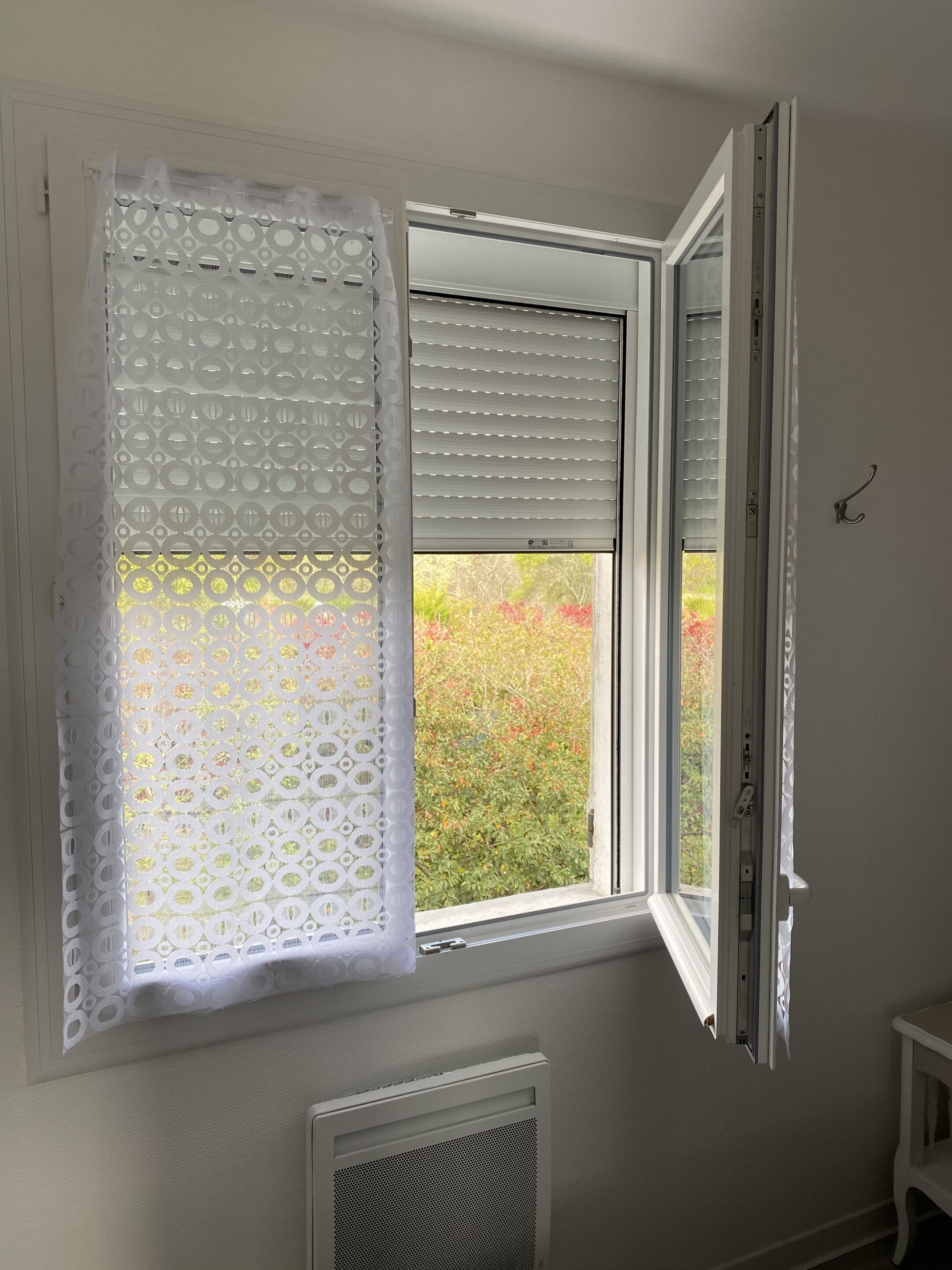 A window with a white curtain and a partially open white blind.