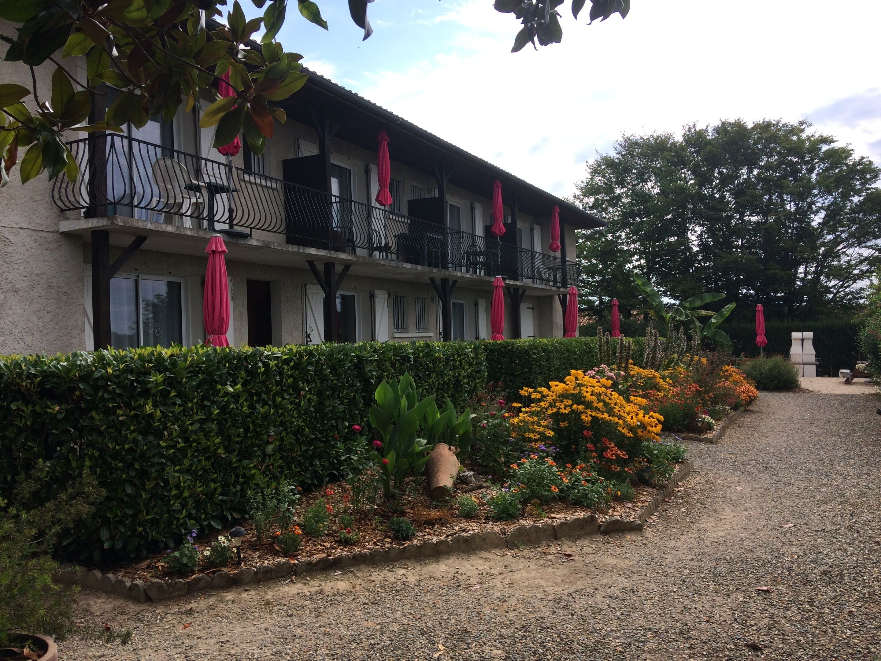A building with a balcony, a gravel path, and a variety of plants and flowers.