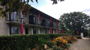 A building with a balcony, a gravel path, and a variety of plants and flowers.