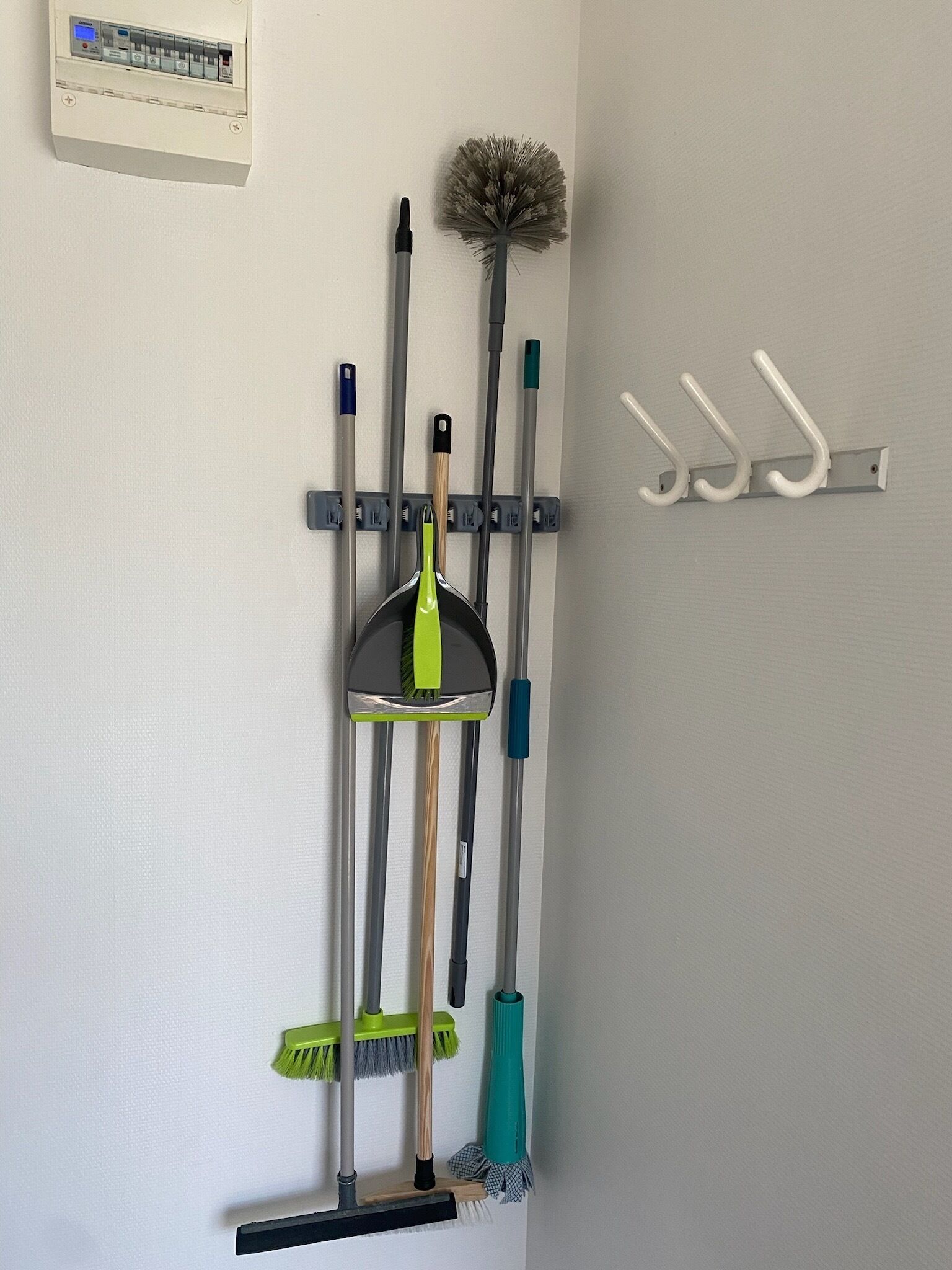 A wall-mounted rack with various cleaning tools, including brooms, mops, and a dustpan.