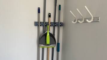 A wall-mounted rack with various cleaning tools, including brooms, mops, and a dustpan.