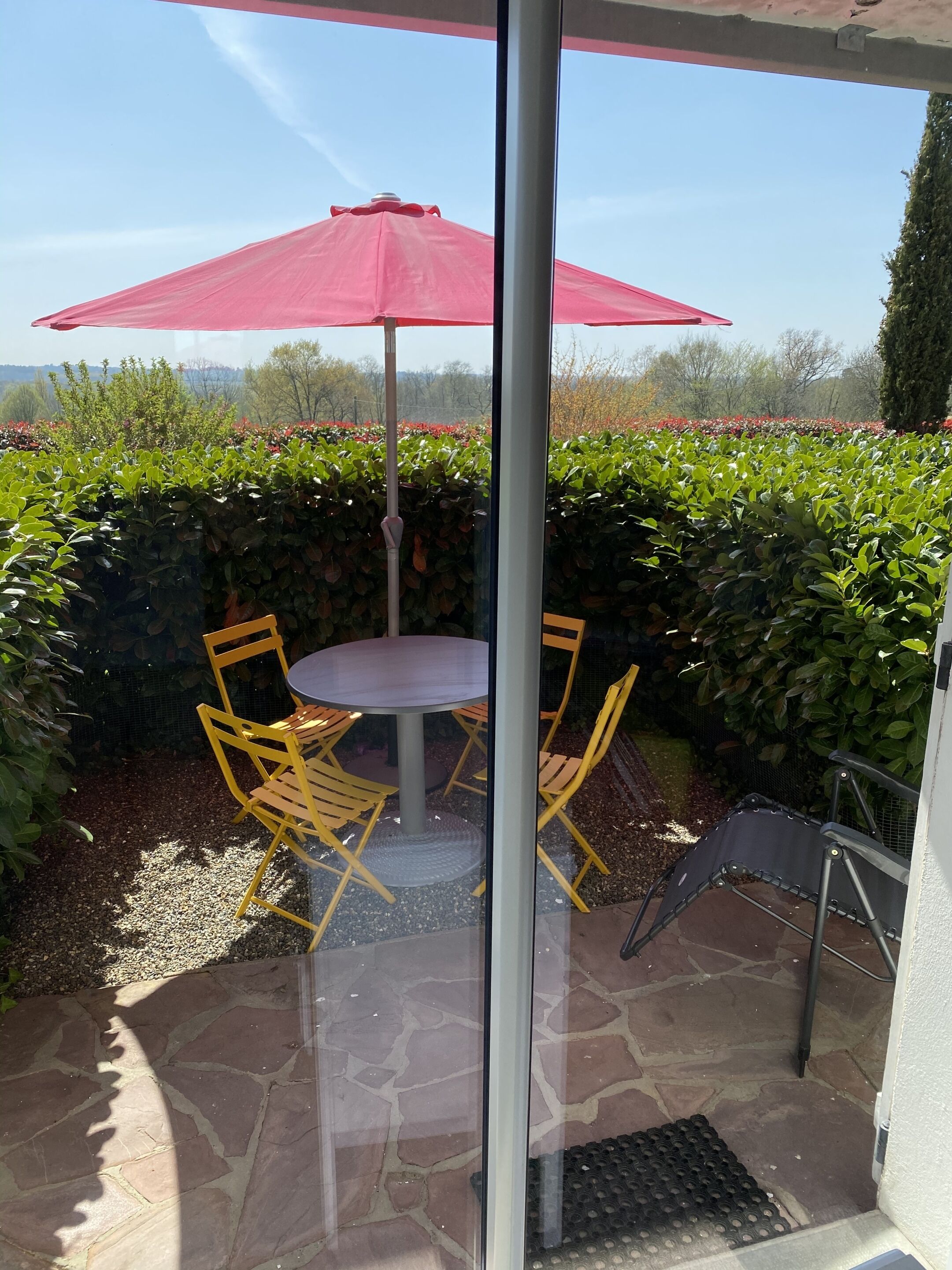 A patio area with a table and chairs, a red umbrella, and a view of a landscaped garden.