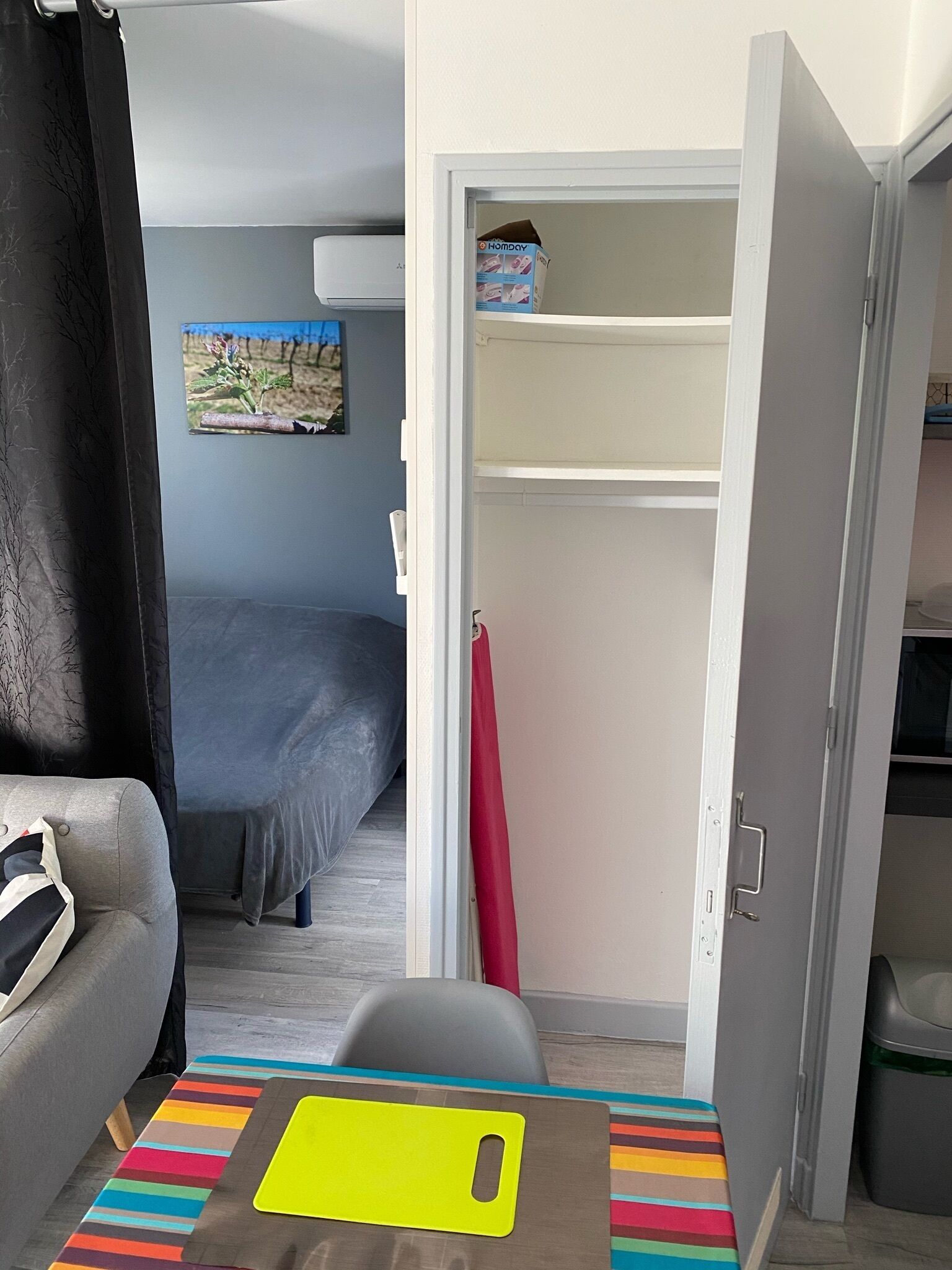 Een compacte kamer met een bed, een klein zitgedeelte en een kast met een rode handdoek.