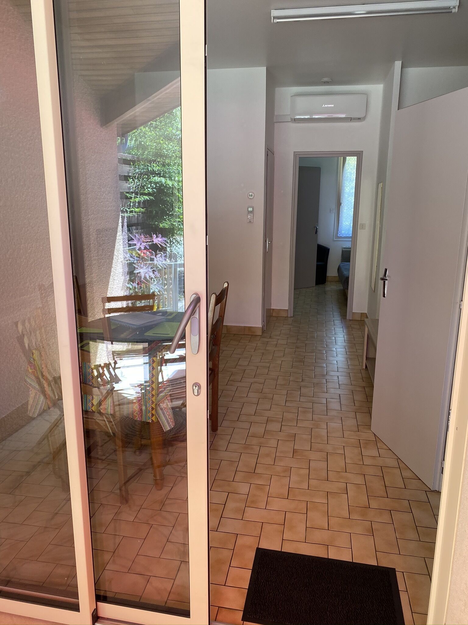 Habitación con puerta de vidrio corrediza que da a un balcón con vistas a zonas verdes. El piso es de baldosas y la puerta tiene un picaporte.