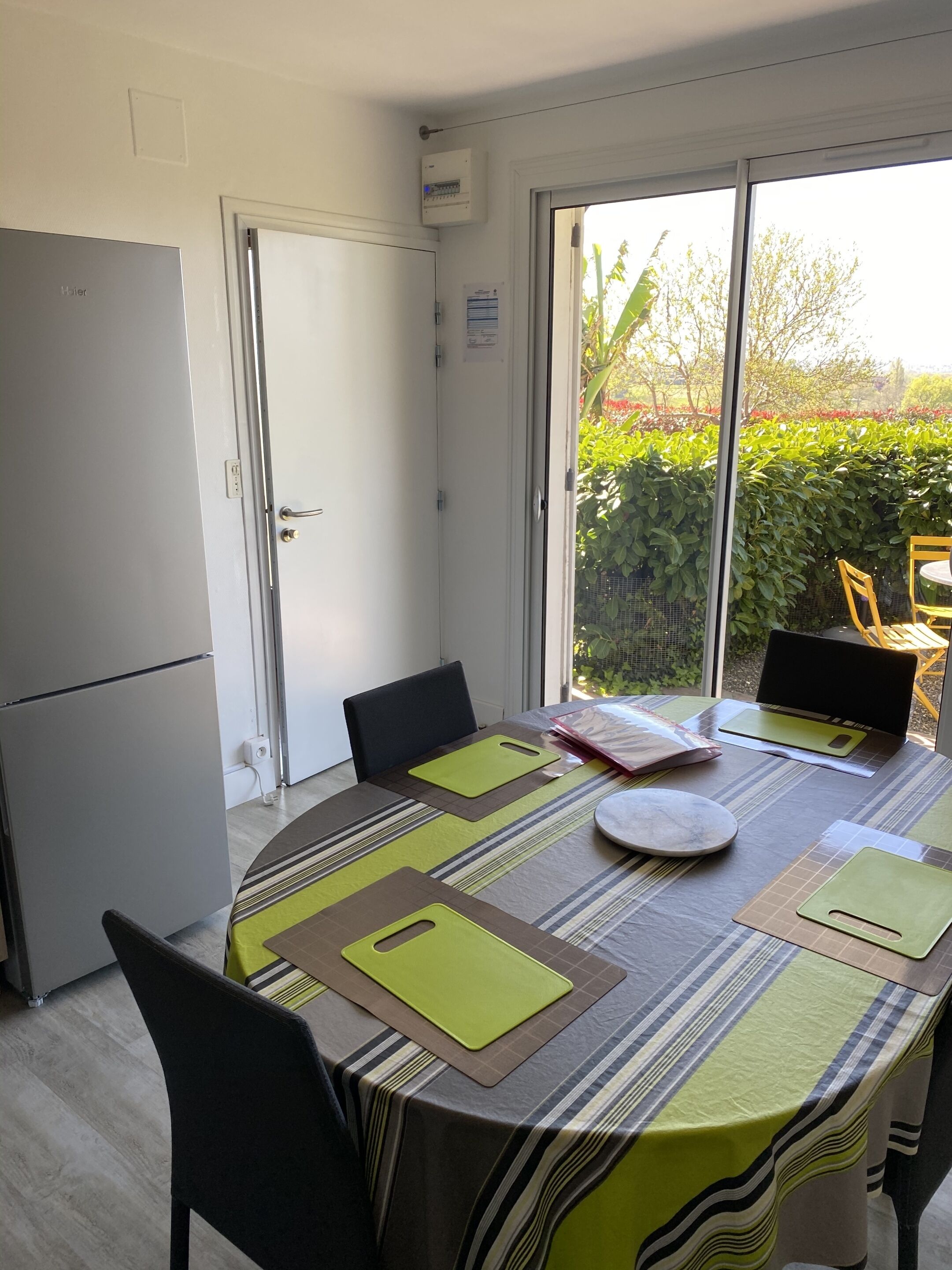Un comedor con una mesa preparada para cuatro, sillas, una computadora portátil y una ventana que ofrece vistas a zonas verdes.