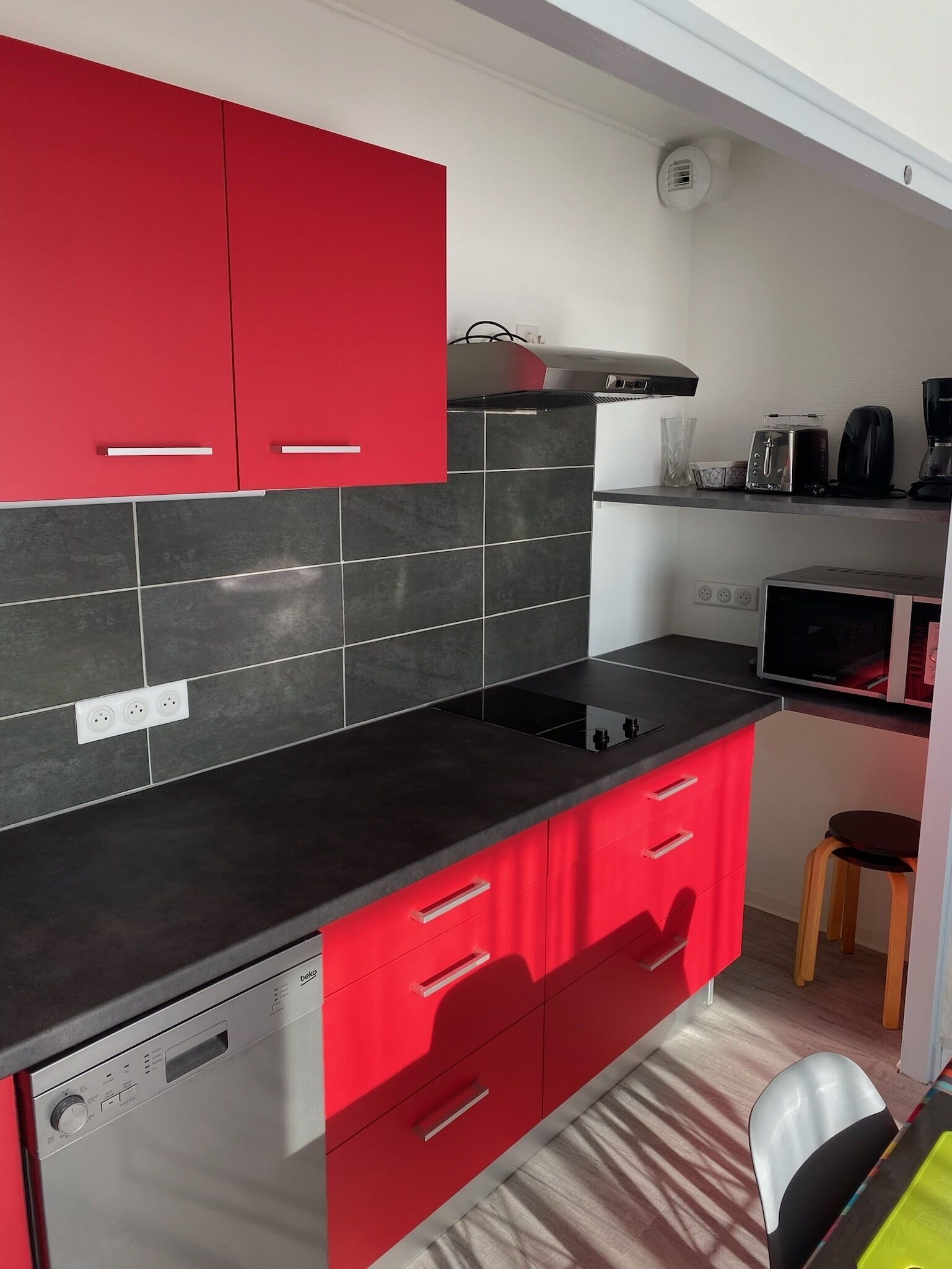 A modern kitchen with red cabinets, a black countertop, and a built-in dishwasher.