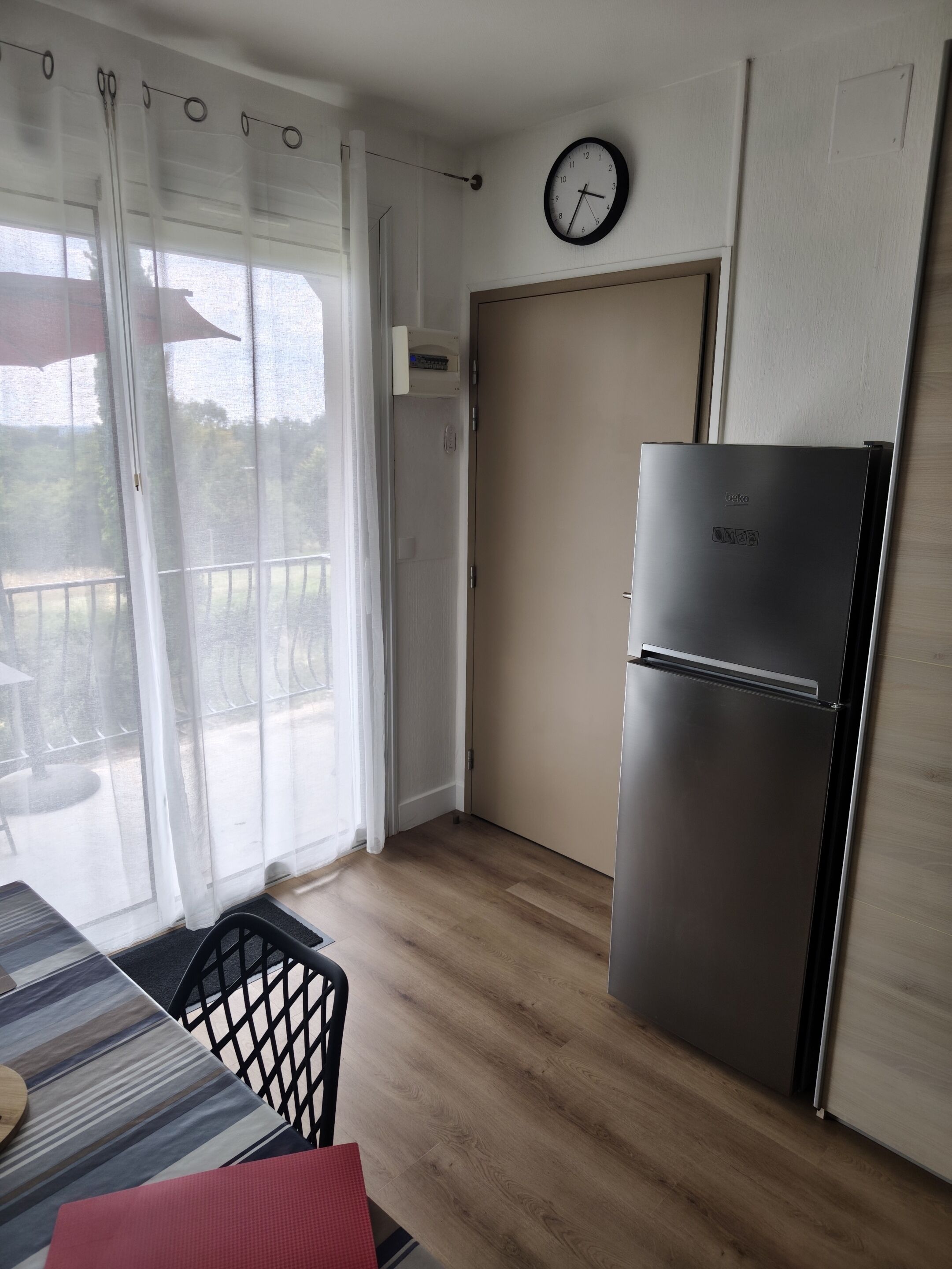 Une cuisine équipée d’un réfrigérateur, d’une table à manger avec des chaises et d’une porte-fenêtre coulissante donnant sur un espace extérieur.