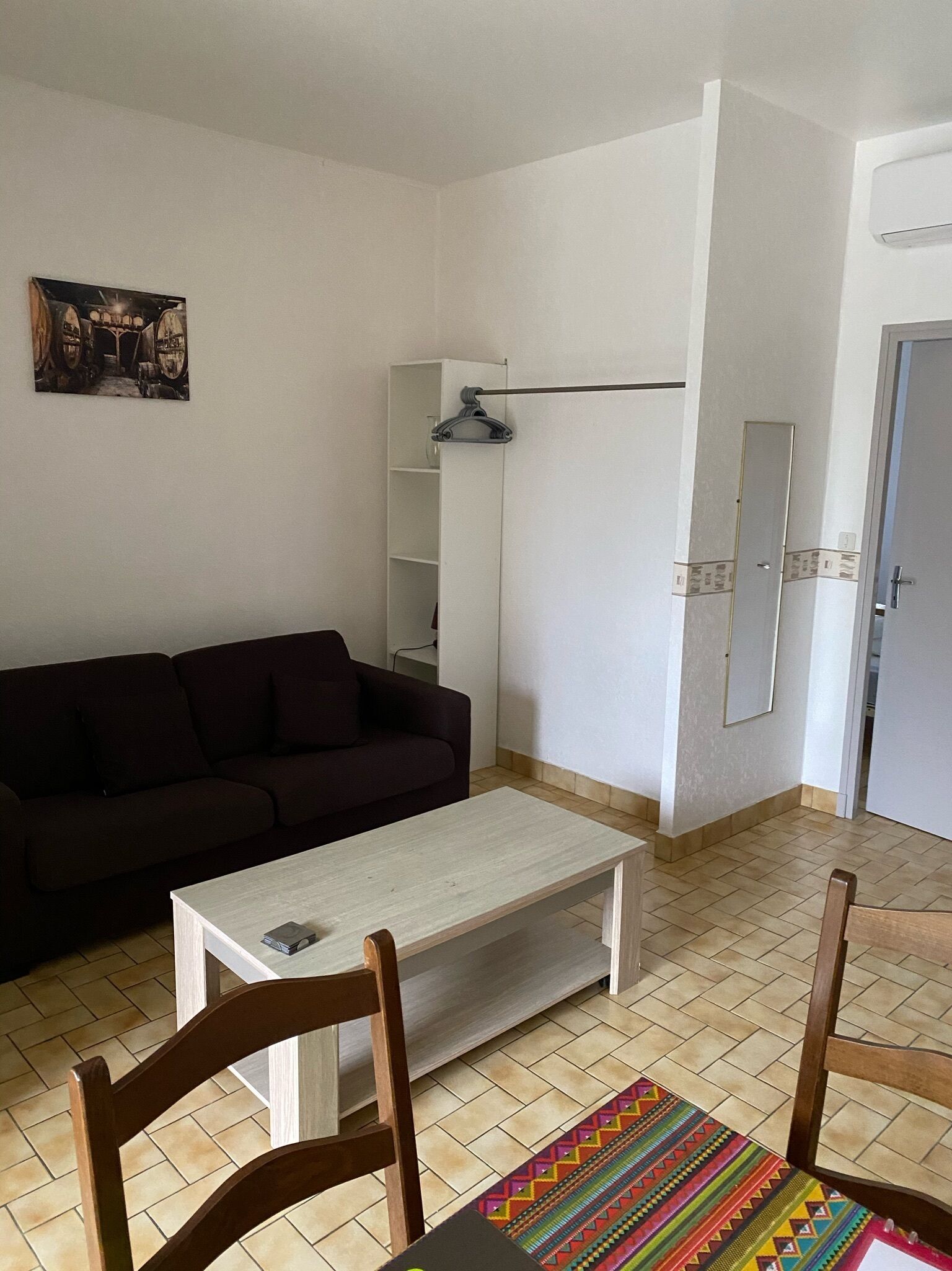A living room with a dark-colored sofa, a white coffee table, and a colorful rug. There is a white cabinet with a mirror and a door, and a painting on the wall.