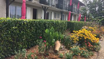 Een hotel met een balkon, een tuin vol planten en bloemen, en een haag.
