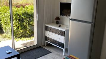A compact kitchen with a refrigerator, a small table, a bench, and a view of greenery outside.