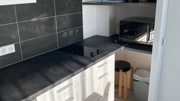 Una cucina compatta con un piano di lavoro nero, mobili bianchi, un forno integrato e un piccolo sgabello.
