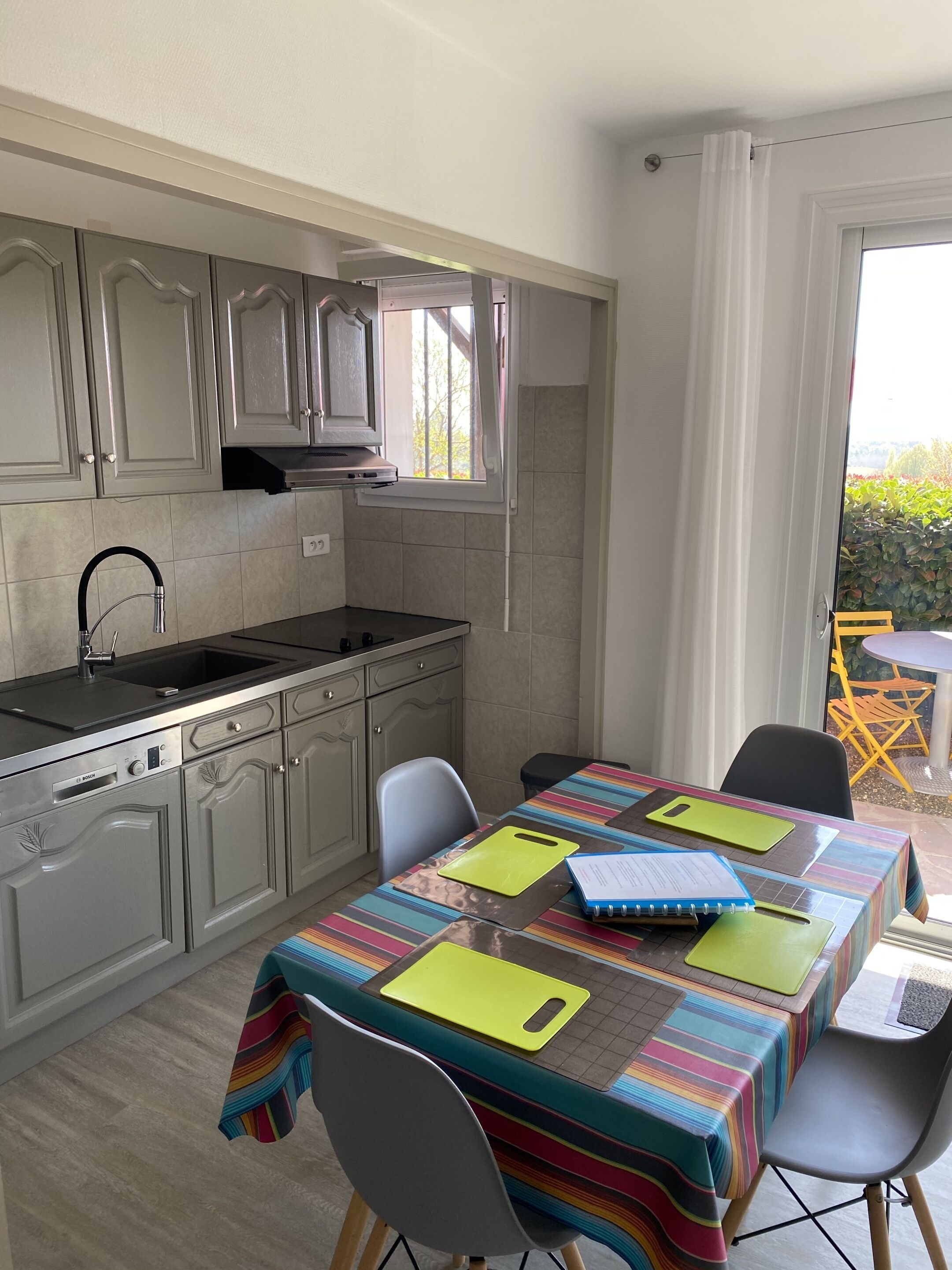 A compact kitchen with a built-in stove, a sink, and cabinets. There is a dining table with chairs and a colorful tablecloth.