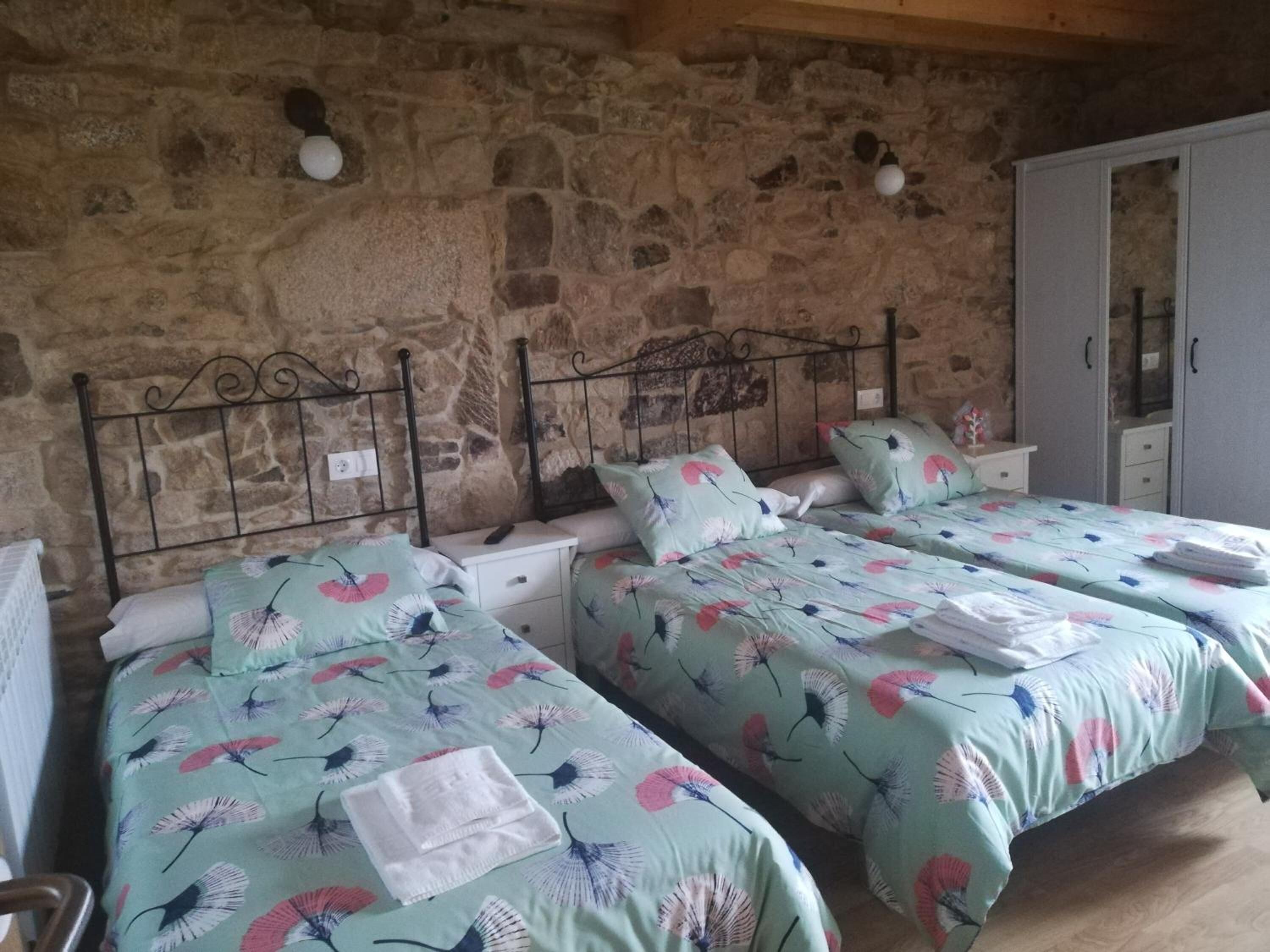 A room with three beds, each with floral bedding, a stone wall, and a wardrobe.