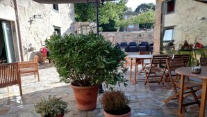 An outdoor patio area with stone flooring, wooden furniture, and potted plants. - Hosteria Calixtino (Palas de Rei)