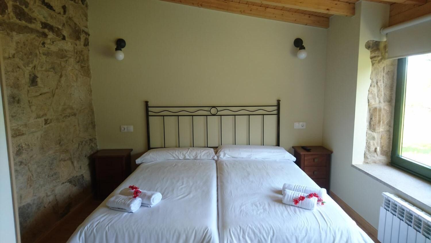 Un lit double avec du linge de lit et des serviettes blanches, un mur en pierre, un plafond en bois et une fenêtre donnant sur un paysage agréable.