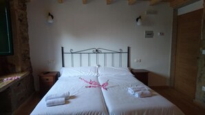 A double bed with white linens, two bedside tables, a wooden headboard, and a stone wall. - Hosteria Calixtino (Palas de Rei)