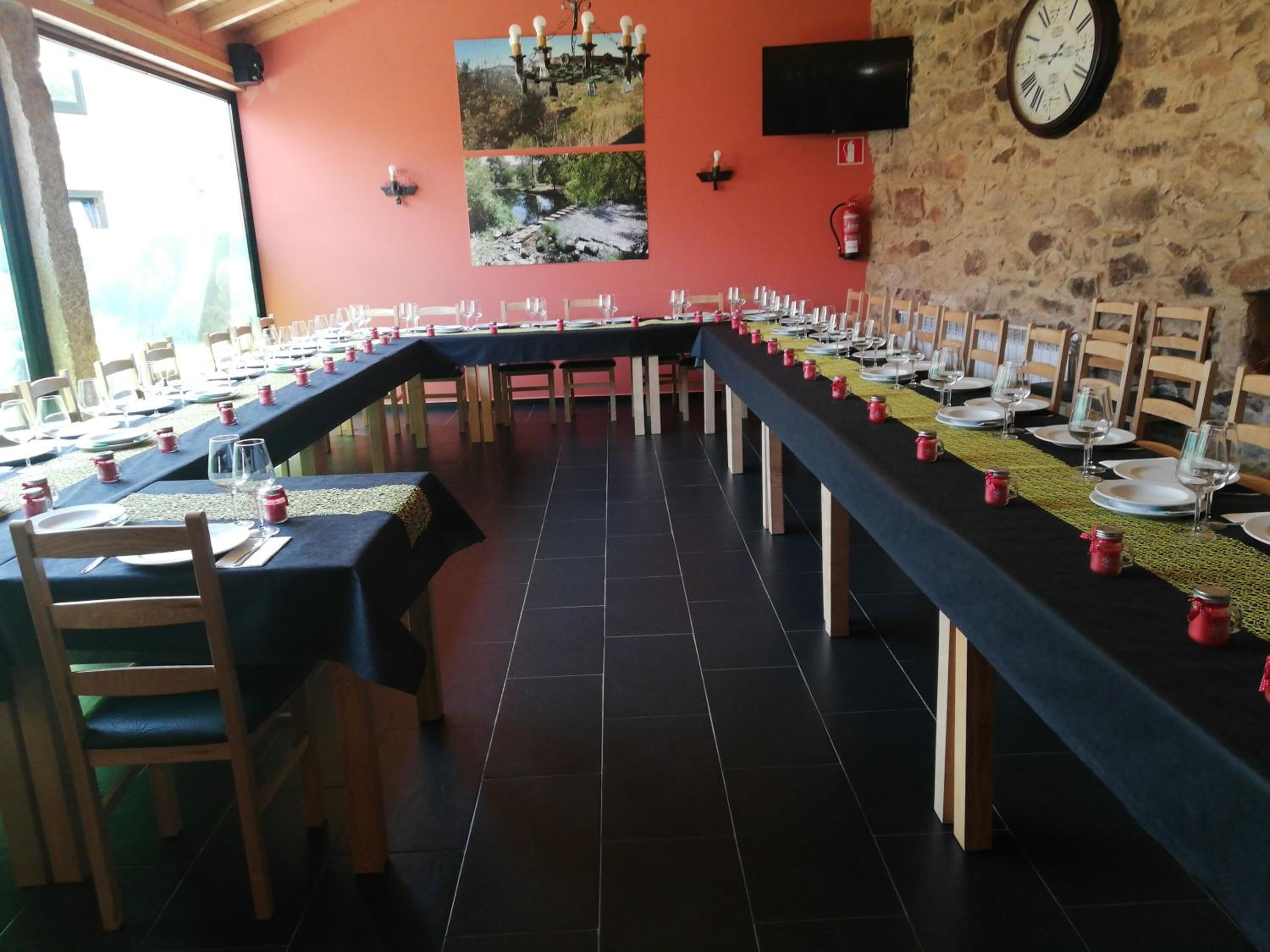 A long dining table set for a meal with chairs, a clock, and a television on the wall.