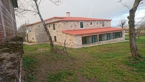 A stone building with a red-tiled roof, large windows, and a grassy yard. - Hosteria Calixtino (Palas de Rei)