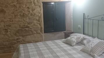Un dormitorio con pared de piedra, una cama con estructura metálica y una puerta.